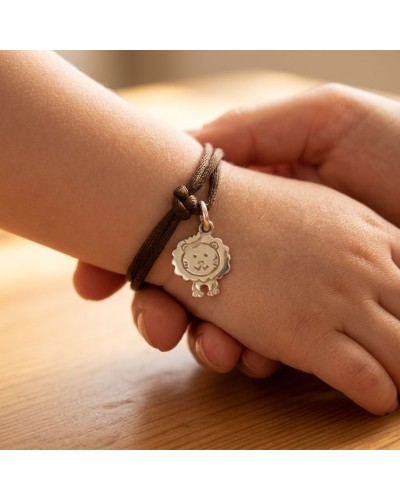 Bracelet simple en cordon brun autour du poignet, avec pendentif rond argenté représentant un lion souriant. Bracelet BB LION.