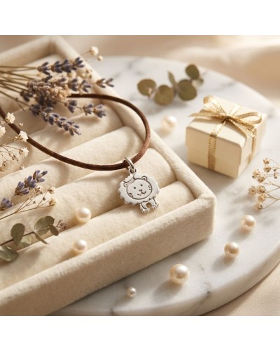 Bracelet BB LION avec pendentif lion argenté sur cordon brun, posé dans boîte en velours crème, décoré de perles et fleurs séché