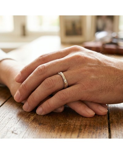 Alliace croisée en or avec diamants sur le doigt de la main masculine, posé sur une table en bois.