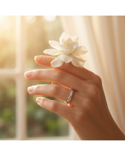 Alliance CROISADE: close-up d'une main portant bague dorée argentée avec une fleur blanche sur fond lumière chaleureuse.