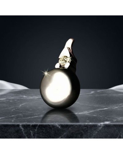Pendentif perle noire brillamment polie avec bijou et petit éclat, posé sur une surface marbrée.