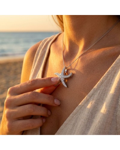 Pendentif étoile de mer argenté orné de petits cristaux, porté sur une chaîne près du décolleté au coucher du soleil.