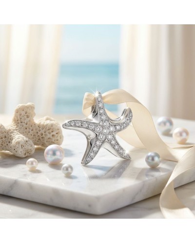 Pendentif ÉTOILE DE MER en argent brillant orné de pierres scintillantes, noué d’un ruban crème sur une surface marbrée avec cor