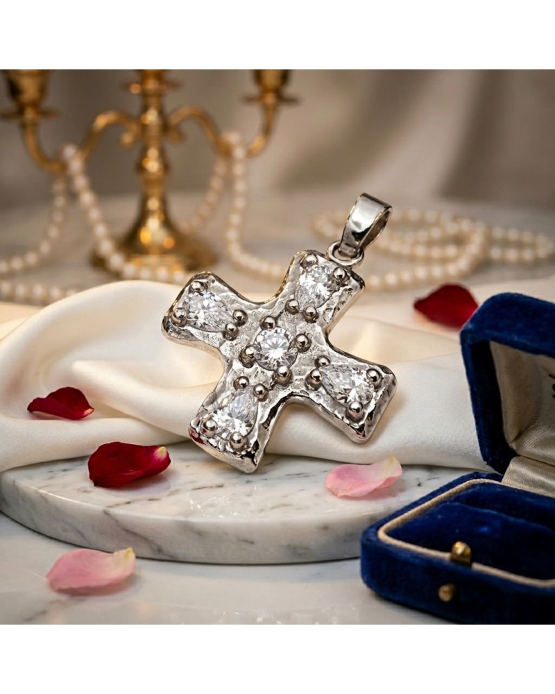 Pendentif croix baroque en argenté orné de brillants, posé sur satin blanc avec pétales roses, casier bleu en arrière-plan. incl