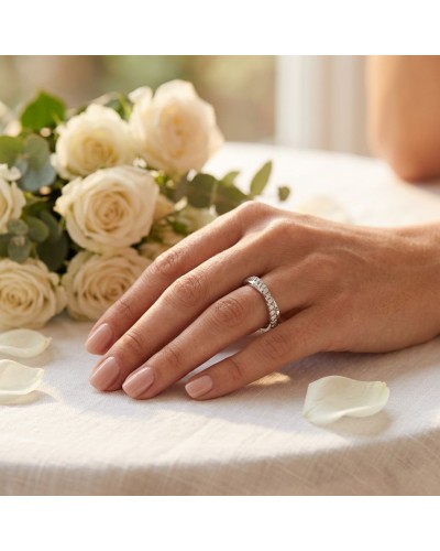 Alliance CROISADE diamants dessus: doigt de femme portant une alliance dorée ornée de diamants, entourée de roses blanches.