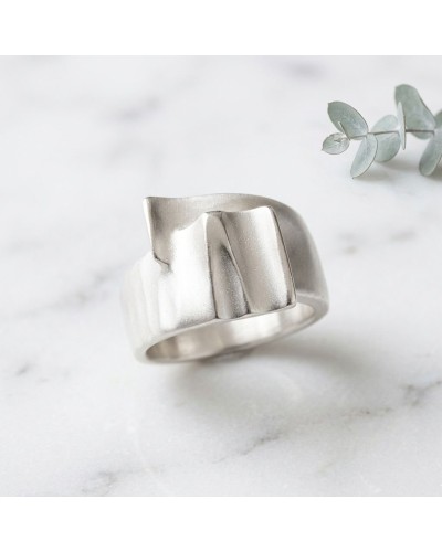 Bague argentée moderne TAFFETAS avec motif géométrique sculpté, posé sur marbre blanc.