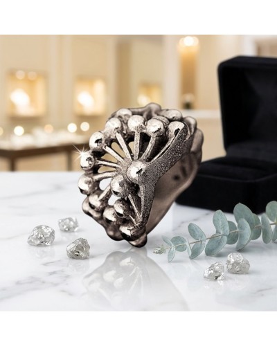 Bague FROGGYLEG argentée à motif florale avec pierres brillantes et pierres sur la table, boîte à bijoux en arrière-plan.