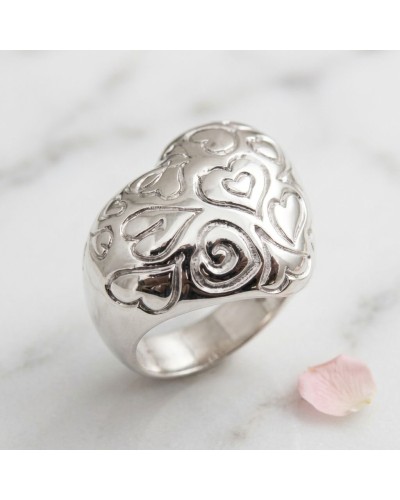 Bague argentée Torsadée en forme de coeurs ajourés, motif romantique sur une surface blanche avec une petite pétale rose à côté.