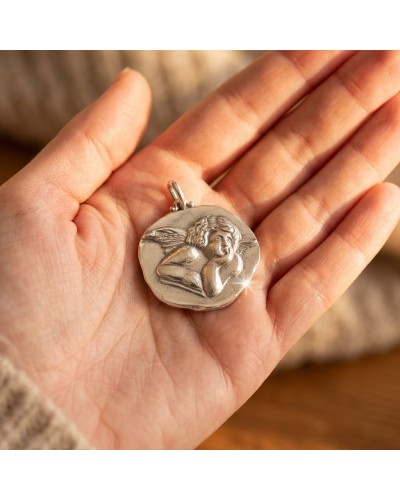 Pendentif ANGE en métal argenté rond, gravé d’un ange allongé posé sur la main montrant les ailes.