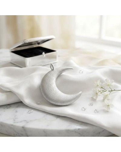 Pendentif lune argenté texturé posé sur un drap blanc avec boîte à bijoux ouverte en arrière-plan.