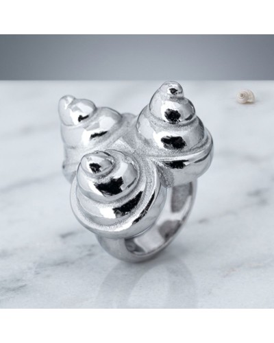 Bague argentée au design sculptural en spirales évoquant des coquillages, portée sur une surface claire - Bague COQUILLAGES.