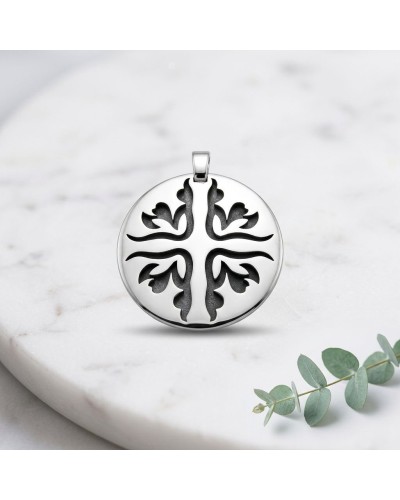 Pendentif rond argenté MATAHARI avec motif arbre stylisé en creux noir, posé sur surface blanche.