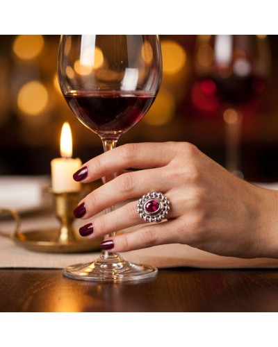 Anneau MARQUISE serti argenté avec pierre rouge sur doigt posé près de verre de vin et bougie.