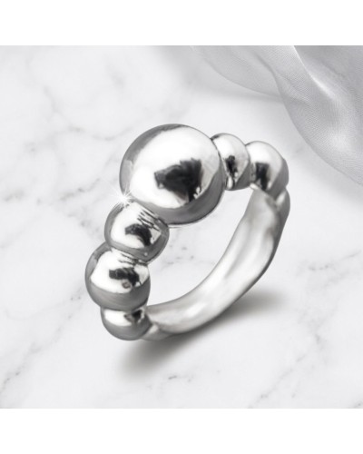 Bague FUSION en argent poli composée de billes reliées, sur fond marbré avec reflet brillant et tissu blanc.