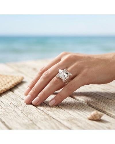 Bague Étoile de Mer en argent avec motif étoile de mer sur doigt posé sur bois près de la plage, reflets brillants.