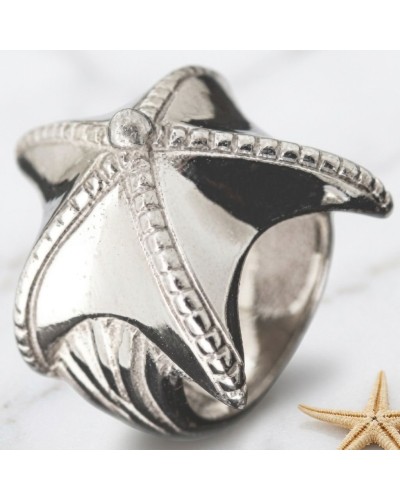 Bague argentée en forme d’étoile de mer gravée, avec détails sculptés et bords décorés, sur fond clair près d’une étoile de mer.