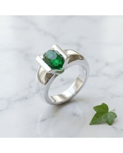 Bague argentée avec pierre verte émeraude taillée, design moderne autour d’un carré incurvé, sur fond marbre. Solitaire BAYA.