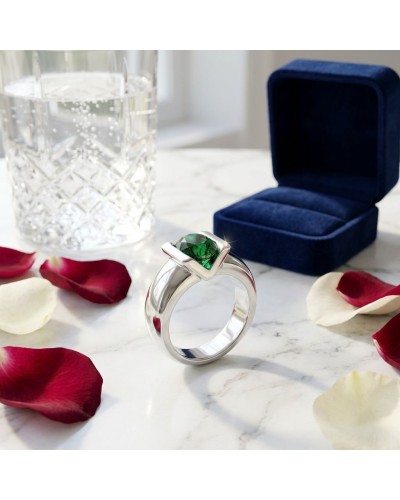 Bague argentée avec pierre green émeraude sur anneau épais, devant boîte bleue velours et pétales rouges et blancs, context Soli