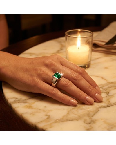 main sujet: une main portant une bague argentée avec pierre verte émeraude, près d'une bougie sur table en marbre (Solitaire BAY