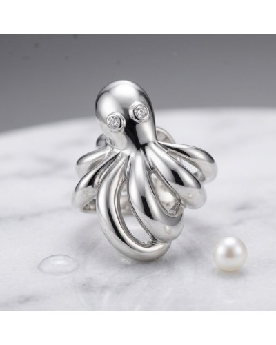 Bague POULPE argentée en forme d’octopus avec tentacules brillantes et deux petits diamants pour les yeux, pose près d’une perle
