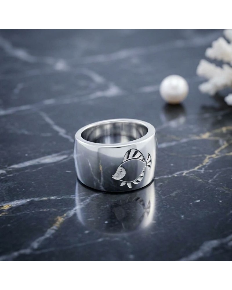 Bague large en argent poli avec motif gravé d’un poisson stylisé "IKAN" sur le côté, posé sur une surface sombre et réfléchissan