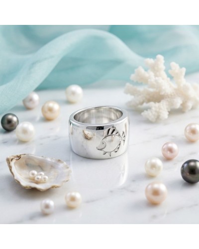 Bague IKAN en argent massif avec gravure poisson, entourée de perles et d’embruns décoratifs sur marbre blanc.