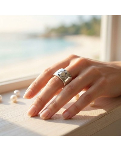 Bague IKAN en argent, large sur le doigt, motif géométrique gravé, fond lumière naturelle près d’une baie.