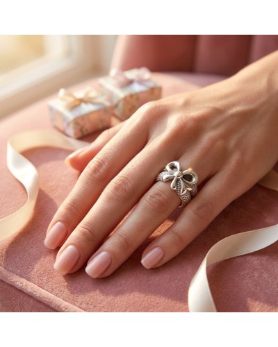 Bague argent bow motif sur doigt, texture pavée légère, pose élégante near pastel gifts et rubans, produit Bague PRESENT.