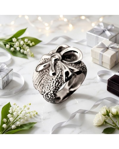 Bague PRESENT en métal argenté avec motif cœur et torsade, entourée de cadeaux et rubans sur marbre blanc.