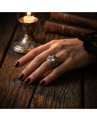 Bague MARGO en argent avec motif swirl sur doigt féminin, manicure bordeaux, près d’une bougie sur une table en bois.