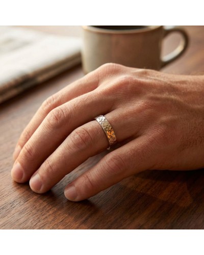 Alliance martelée pour homme en or porté sur l’annulaire, près d’une tasse sur une table en bois.