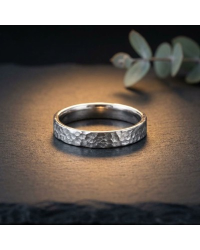 Alliance effet martelé pour homme en or: bague argentée martelée posée sur surface sombre avec branche de feuillage en arrière-p