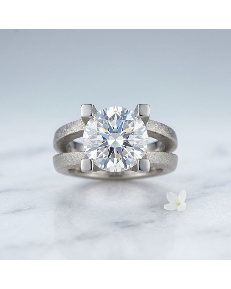 Bague ROMANTIS en argent ou métal gris avec solitaire rond brillant et fourchette à quatre griffes, pose minimaliste sur marbre.