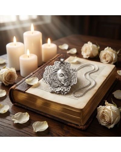 Pendentif croix en argent texturé représentant Jésus posé sur une Bible ancienne, chaîne argentée autour, bougies et roses blanc