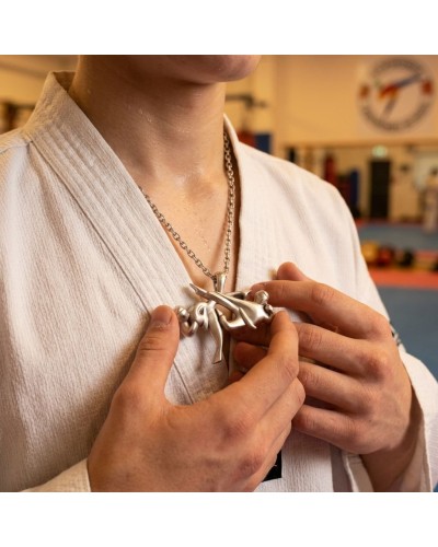 Pendentif Taekwondo argenté suspendu à une chaîne, porté par une personne en karatéka, chaînette visible.