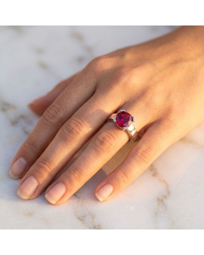 Bague HASRAT: anneau argenté avec pierre rouge ronde facettée portée sur doigt sur fond clair.