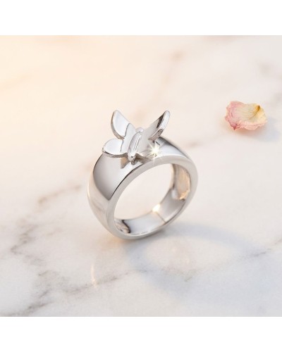 Alliance KUPU-KUPU: bague argentée brillante avec pendentif papillon en détail sur fond marbré, pétale pastel à côté.