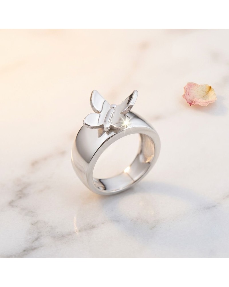Alliance KUPU-KUPU: bague argentée brillante avec pendentif papillon en détail sur fond marbré, pétale pastel à côté.