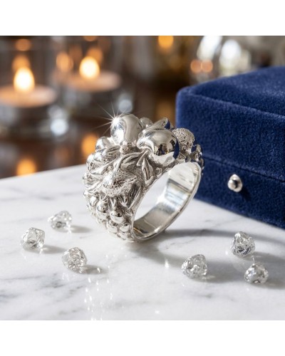 Bague argentée sculptée en forme de grappes, ornée de petits éclats, sur surface blanche avec boîte bleue en arrière-plan.