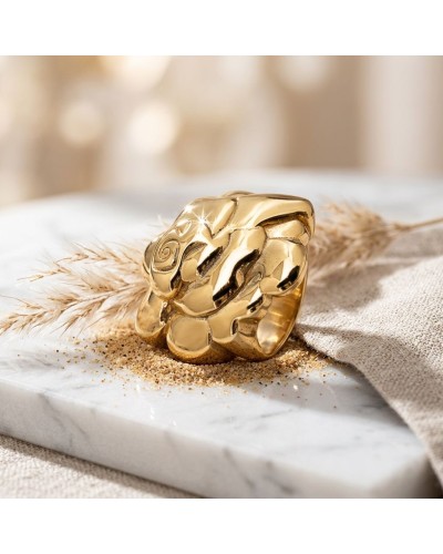 Bague SABLE en or massif avec motif florale gravé, posée sur une surface blanche avec du sable et des brins de paille.