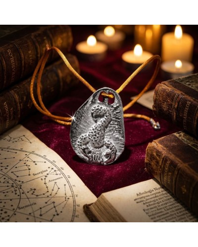 Pendentif zodiaque Scorpion en métal argenté avec cordon orange, posé parmi des livres anciens et des bougies allumées.