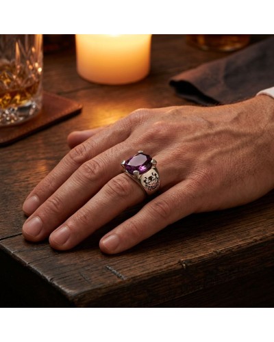 Chevalière SUMATRA pierre violette facettée sur doigt masculin, détail gravure sombre sur le métal argenté près d’une table en b
