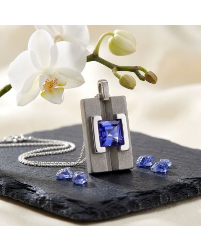 Pendentif moderne en argent avec pierre bleu vif carré, collier argenté et orchidée blanche en arrière-plan. Pendentif MASA DEPA