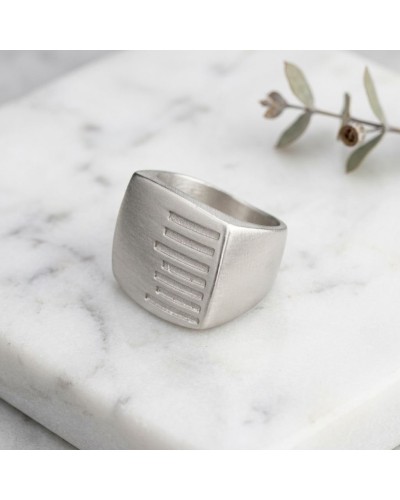 Bague KEKAYAAN en argent mate, large ouverte avec motif de lignes gravées sur le devant, posée sur marbre blanc.