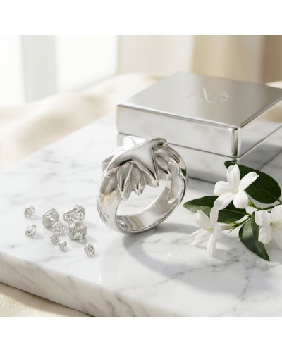Bague éclipse argentée with star-like sculpted design, near diamonds, white flowers, and metallic box on marble surface.