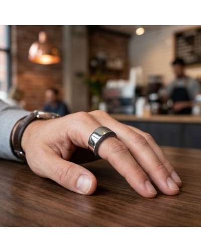 Bague CLEAN argentée brilliante portée sur l’annulaire d’une main masculine posée sur une table en bois, intérieur de café en ar