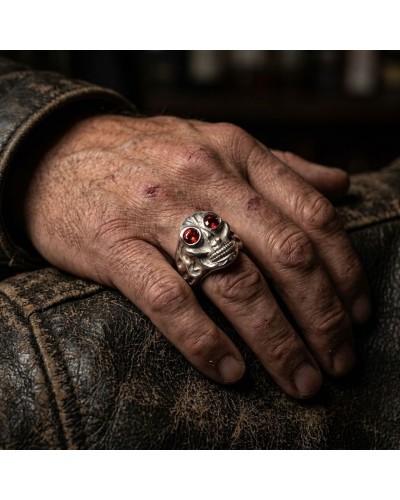 Bague CORSAIRE en argent gravée en forme de crâne avec deux yeux rouges, portée sur une main rugueuse et porrée.