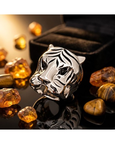 Bague tigre argentée au fini brillant, motif zébré noir et blanc, posée sur une surface noire avec pierres amber et bijoux autou