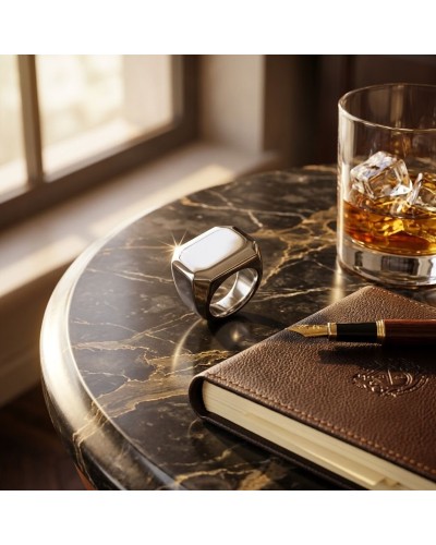 Chevalière MAOUSSE posée sur une table en marbre près d’un carnet en cuir et d’un verre de whisky avec glaçons, éclat reflété su