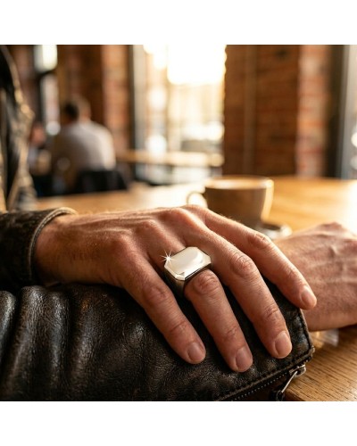 Chevalière MAOUSSE brillante sur le doigt d’un homme posé sur une table en bois dans un café.